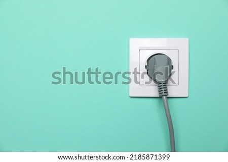 Power socket with inserted plug on turquoise wall, space for text. Electrical supply Royalty-Free Stock Photo #2185871399