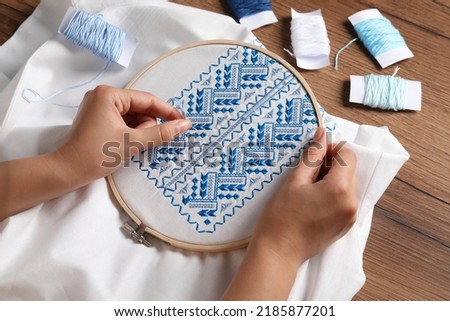 Woman embroidering white shirt with blue thread at wooden table, above view. Ukrainian national clothes Royalty-Free Stock Photo #2185877201