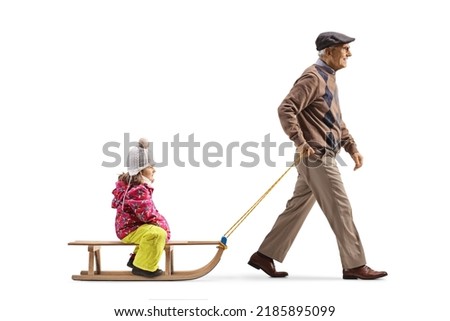 Full length profile shot of a grandfather walking and pulling a girl on a sled isolated on white background
