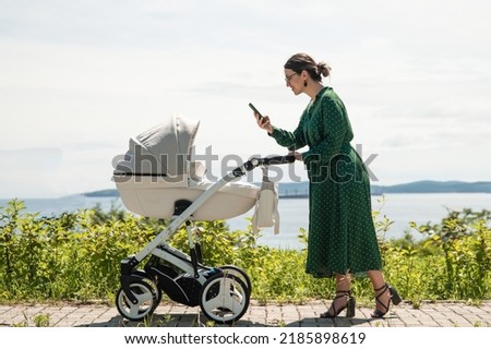 A young mother in a green dress walks with her baby. Mom takes a picture of a baby in a stroller while walking in the city.