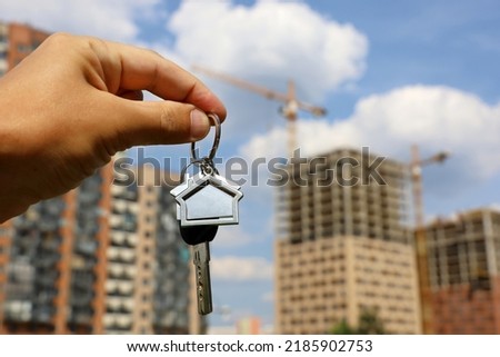 Real estate agent, keychain in shape of a house and key in male hand on background of construction cranes and new buildings. Byung apartment or renting property in summer Royalty-Free Stock Photo #2185902753