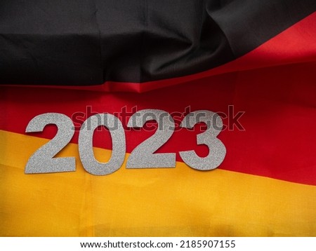 2023 on the background of german flags. 2023 silver figures lie on flag with black, red and yellow backdrop. Christmas and New year card. Germany concept of celebrating winter holiday