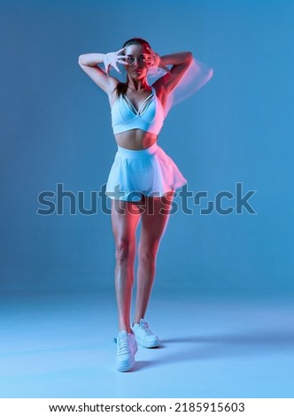 A beautiful tanned girl stands and with hands behind head. Studio portrait on a blue background with a bluer effect