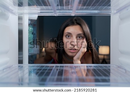 Shocked young woman looking in the empty fridge, she has no food at home, point of view shot from inside the fridge Royalty-Free Stock Photo #2185920281
