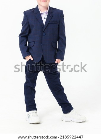 Boy teenager in a school uniform on a white background. A schoolboy demonstrates black trousers with a belt, a jacket, a white shirt and white sneakers. Vertical photo