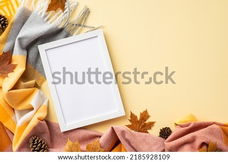Autumn concept. Top view photo of white photo frame yellow maple leaves pine cones and plaid on isolated pastel beige background with empty space
