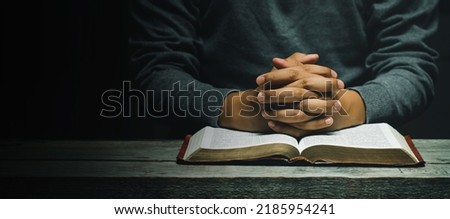 Hand of man while praying for the Christian religion, Man praying with his hands together with Bible on a wooden table. begging for forgiveness and believing in goodness. copy space for banner