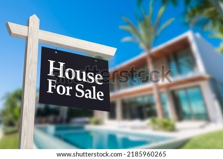A dark for sale sign in front of a contemporary modern house with swimming pool. Real estate concept.