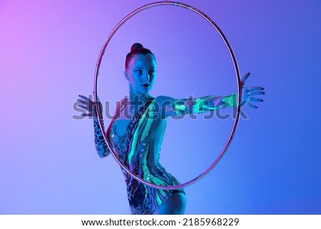 Portrait of young, muscular girl, female rhytmic gymnast training with hoop isolated over blue pink studio background in neon light. Concept of action, motion, sport life, motivation, competition. Royalty-Free Stock Photo #2185968229