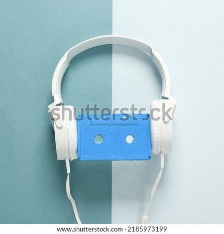 Stereo headphones with audio cassette on blue background. Retro 80s still life. Top view
