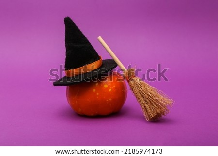 Halloween stil life. Pumpkin with Witch hat and broom on purple background