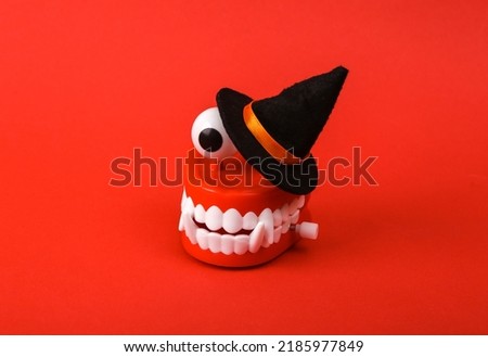 Funny toy clockwork jumping teeth monster with eyes and witch hat on red background. Halloween still life
