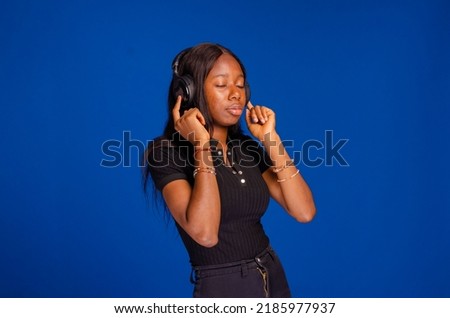 Gorgeous brunette lady listening music in headphones and singing on blue background