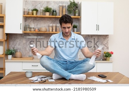 Stressed man sitting on the table and holding many bills in his hands in a spending, taxes and debt concept Royalty-Free Stock Photo #2185980509
