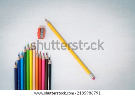 Colored crayons, a pencil with eraser and a pencil sharpener are resting on a white wooden table, concept of back to school for children, free space for text.