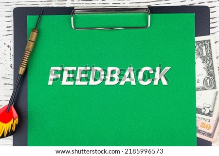 FEEDBACK - word (text), a dart for darts and dollar bills on a green background of a notebook, a wooden white table. Business concept: buying, selling, commerce (copy space).