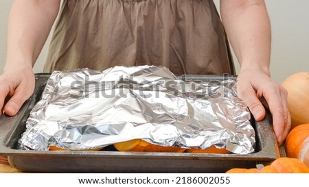 Pumpkin slices close up on a prepared baking pan covered with aluminum foil. Baking pumpkin, step by step pumpkin puree recipe, lifestyle, woman hands Royalty-Free Stock Photo #2186002055