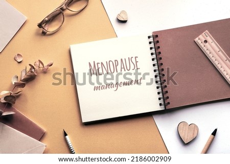 Caption motivator text Menopause management in square album, notebook with spiral binder. Wooden pen, dry eucalyptus twig, wooden heart shape. Soft natural light. Monochromatic beige color hues.