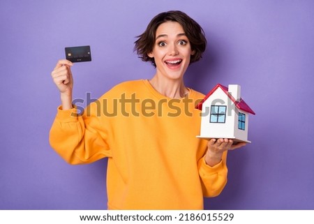 Photo of astonished attractive girl hold debit plastic card small house isolated on violet color background