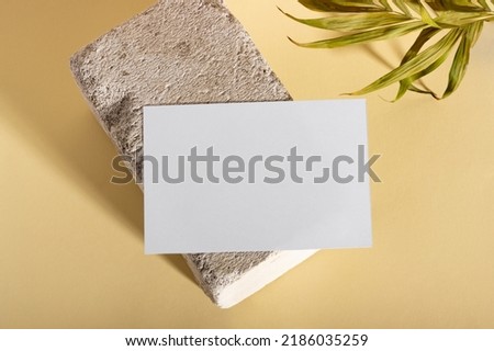 Mockup with blank horizontal paper cards with copy space on a plinth with palm leaves. Hard sunlight and shadows on a beige background. Minimal template for business layout. Top view, flat lay