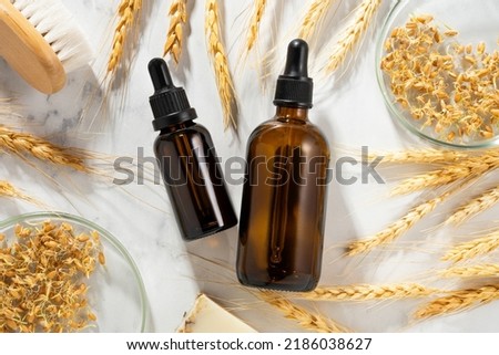 Conceptual composition of wheat essential oils and wheat germ on a marble table. Oil with serum for skin and hair care. Dark glass bottles of body oil with a dropper. Selfcare and wellness. Top view. Royalty-Free Stock Photo #2186038627