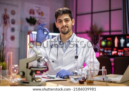 Male scientist working in laboratory. Young indian man researcher supervisor are doing investigations with test tubes while writing research results