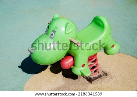 Rocking chair on a green metal spring made of plastic in the shape of a hippo on a playground with a rubberized coating. Kids sports hobbies.