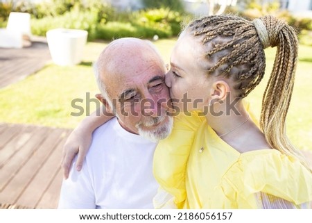 Little girl kisses her grandfather, an elderly man hugs his granddaughter. Caucasian. Summer time. Concept of happy old age, family, generational relationships, happiness, love, childhood, retirement.