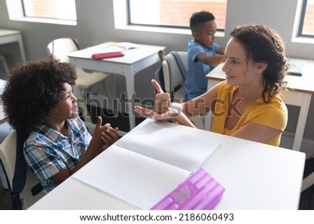 Caucasian young female teacher teaching sign language to african american elementary boy in class. unaltered, education, childhood, learning, teaching, disability, communication and school concept.
