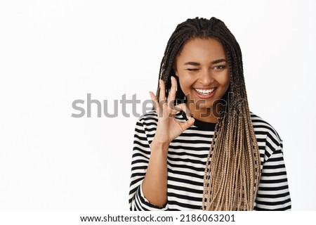 Smiling happy black girl wink, shows okay ok sign, approve, recommends store or company, complimenting smth, standing over white background