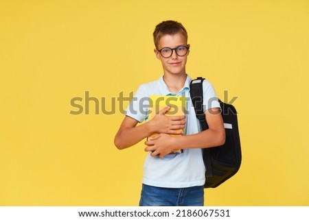 Portrait of a schoolboy in glasses with textbooks and a backpack on a yellow background. Back to school