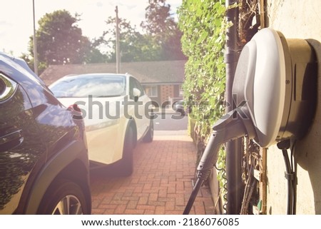 Electric car plugged in to charge outside home with power cable Royalty-Free Stock Photo #2186076085