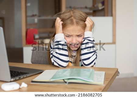 Caucasian little girl suffering from headaches, migraines, overwork, too many homework assignments online indoors. A tired schoolboy, a crying child Royalty-Free Stock Photo #2186082705