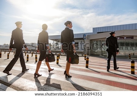 Flight attendants with bags and pilots crossing the road in the airport Royalty-Free Stock Photo #2186094351