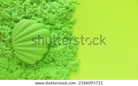 Seashell sand figure made of green kinetic sand on light green paper background with place for text. Kids sensory game, development fine motor skills. Leisure and fun time on summer holidays concept. Royalty-Free Stock Photo #2186095721