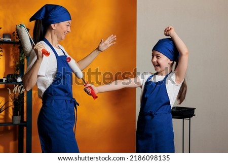 Young people painting orange wall with paintbrush roller tools, having fun together redecorating apartment room. Woman and young child doing diy renovation work, renovating home with paint.