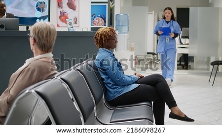 Asian nurse taking african american woman to do checkup visit with doctor in medical office. Female patient waiting in hospital reception lobby to start consultation appointment.
