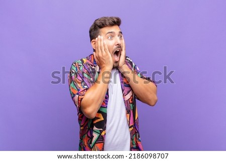 young man feeling happy, excited and surprised, looking to the side with both hands on face Royalty-Free Stock Photo #2186098707