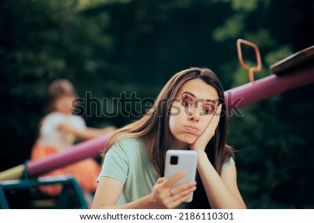 
Bored Mom Using Smartphone Supervising her daughter at the Playground. Mother overusing technology while babysitting in the park
