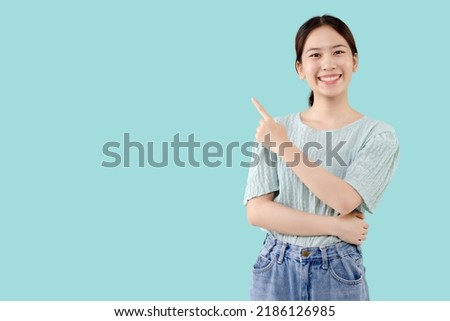 Asian pretty girl standing over isolated mint green background pointing finger to the side with copy space.