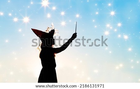Black silhouette of witch with magic wand isolated on fairy star sky background.Beautiful young woman in black robe and wizard hat conjuring, making witchcraft. Halloween party art design.Copy space 