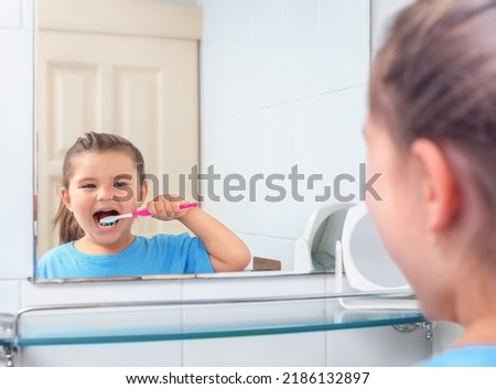 Girl brushing her teeth looking in the mirror in the restroom