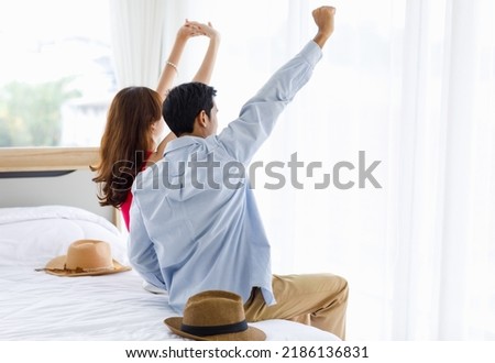 Asian unrecognizable unknown male female husband and wife traveler lover couple in casual outfit sitting stretching arms up while arriving at hotel bedroom resting relaxing in summer vacation weekend. Royalty-Free Stock Photo #2186136831