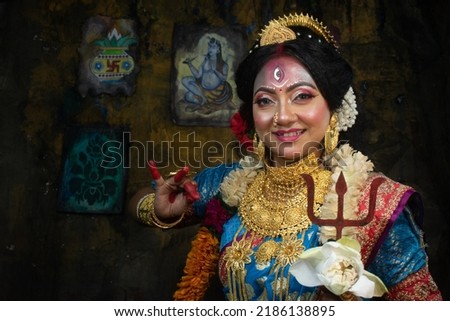 Concept Agomoni shoot with black haired Indian brunette woman face with perfect makeup and wearing jewelers with traditional dress like goddess