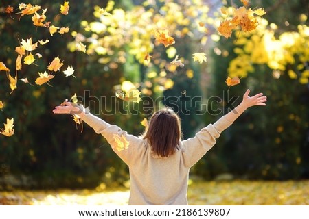 Young woman is having fun while walking through the forest on a sunny autumn day. Girl plays with maple leaves and throws them up. Fallen leaves rustle. Royalty-Free Stock Photo #2186139807