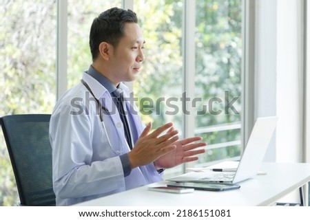 Asian senior doctor sitting in medical office while video call meeting using laptop computer.