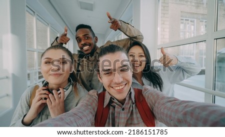 Point of view of four positive multi-ethnic group of friends talking selfie photos holding smartphone and having fun laughing while standing in corridor of university.