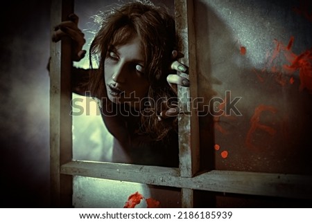 Horror scene. A scary ghost girl looks out of the window of an old abandoned house. Haunted house. Halloween. Royalty-Free Stock Photo #2186185939