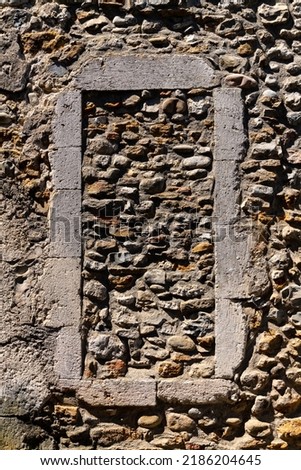Weathered old stone frame of a bricked up window in a rough stone wall facade of a typical house in Vallon-Pont-d'Arc, Provence, southern France. Background illuminated by bright summer sunlight.