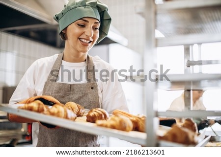 Female baker at the kitchen holding freshly baked croiisants Royalty-Free Stock Photo #2186213601